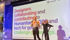 Eriol standing on stage in front of a slide that reads 'Designers collaborating and contributing to Humanitarian OSS and tech for good at challenge gatherings.'